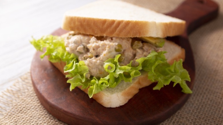 A tuna salad sandwich with lettuce and bread, sitting on a wooden board