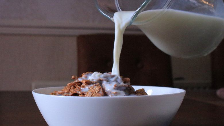 A jug of milk being poured over a bowl of cereal