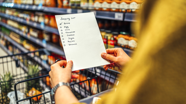 Person holding grocery list and pushing cart