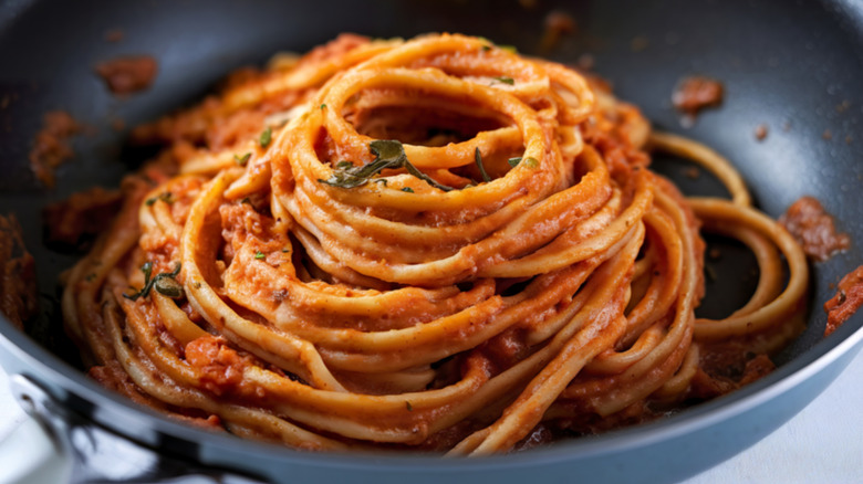 Mound of spaghetti with tomato sauce inside black steel pan
