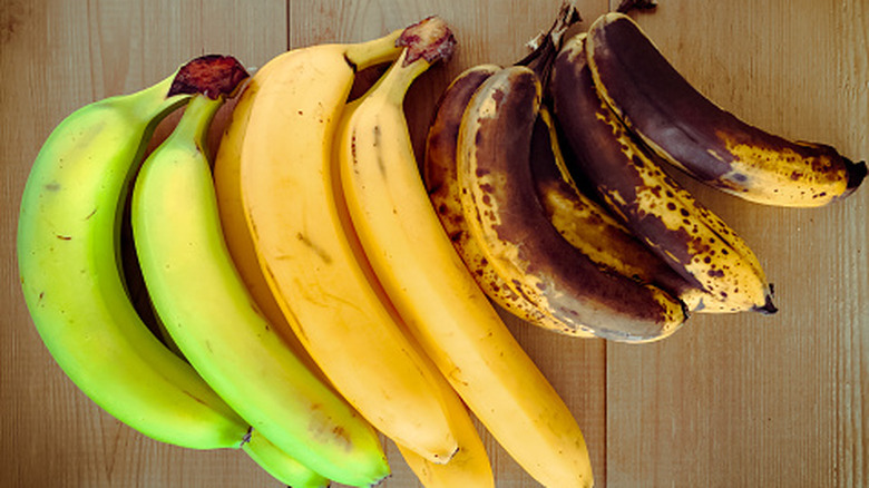 Three bunches of bananas at three ripeness stages: green, yellow, and browning.