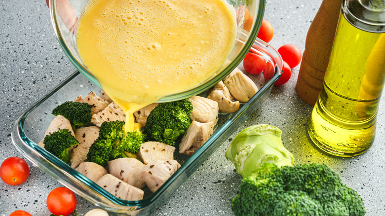 Overhead view of pouring whisked eggs into a casserole dish with meat and veggies