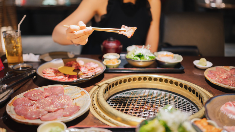 Person dining at Korean BBQ holding meat with chopsticks.