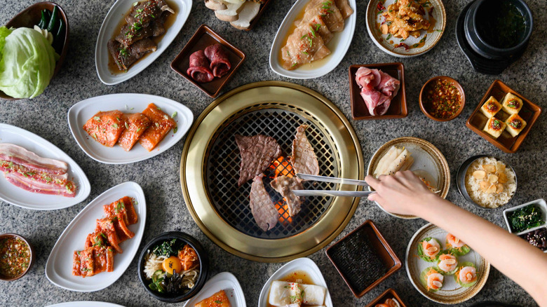 Food items on a Korean BBQ grill surrounded by raw food items on plates.