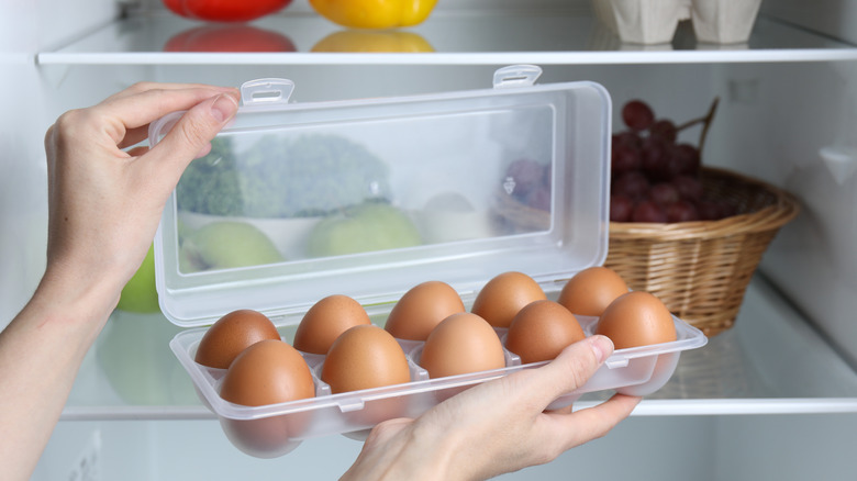 Someone opens up a plastic container of eggs in front of an open fridge