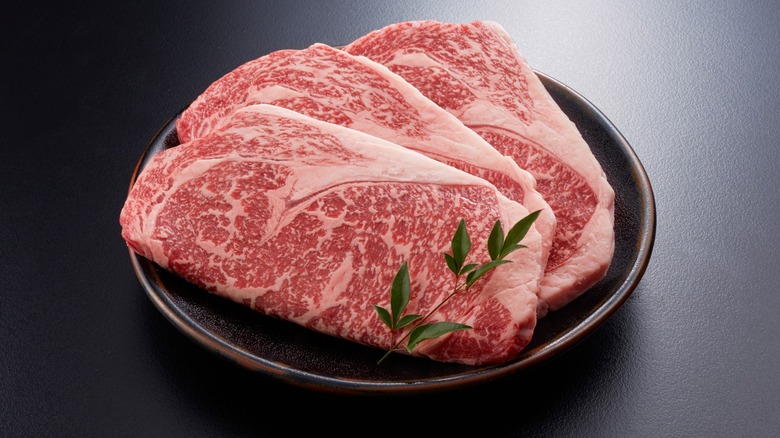 several deeply marbled raw wagyu steaks on a plate