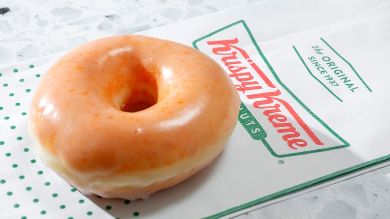 Krispy Kreme glazed donut sitting on white napkin with Krispy Kreme logo