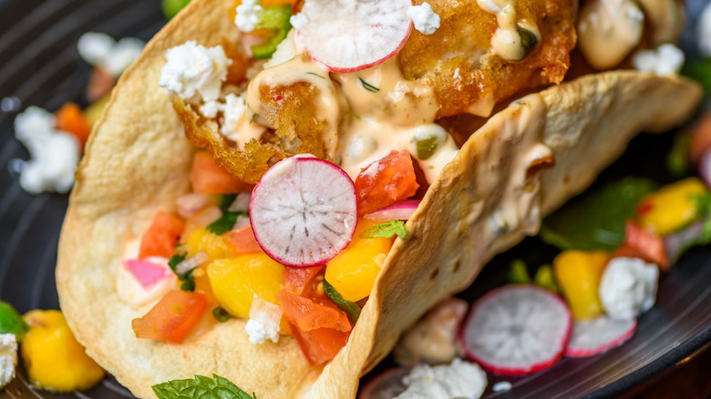A fish taco with spicy crema, mangoes, and radishes