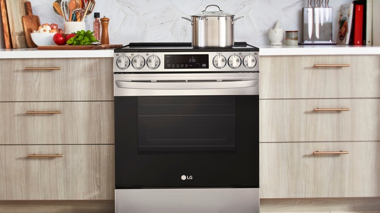 LG brand stainless steel and black range and oven inside kitchen with wooden drawers and various cooking tools on counter