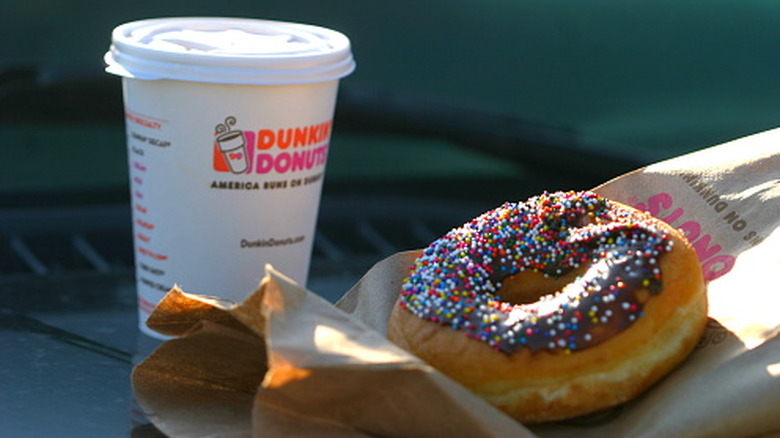 A branded Dunkin' Styrofoam coffee cup and a chocolate glazed donut, resting on a branded paper bag