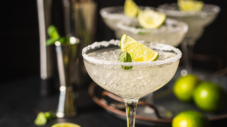 Margarita cocktail with lime and ice on dark wooden table.