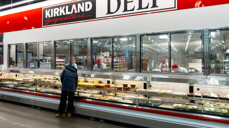 Costco store's Kirkland deli section with large red sign and display cases of foods