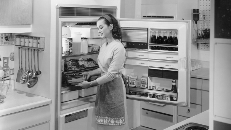 Black and white photo of 1950s woman stocking a refrigerator