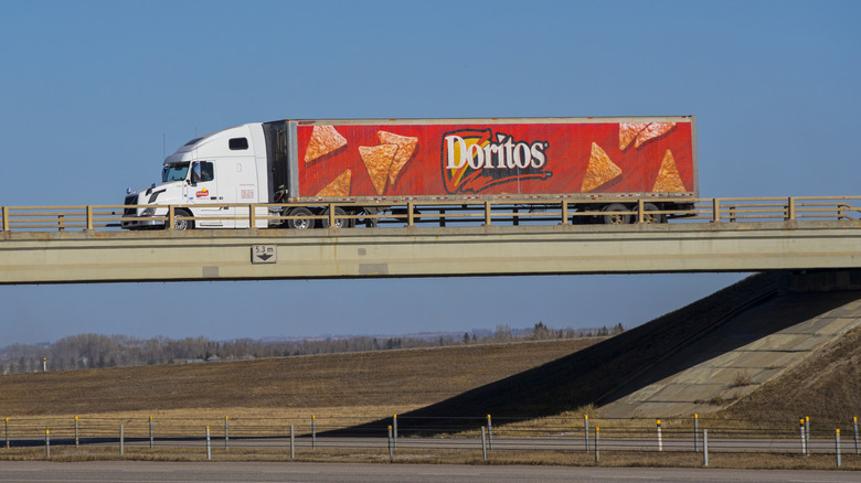A Doritos branded truck crosses a highway bridge in front of a blue sky