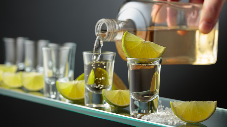 close up of hand pouring tequila shots with lime and salt