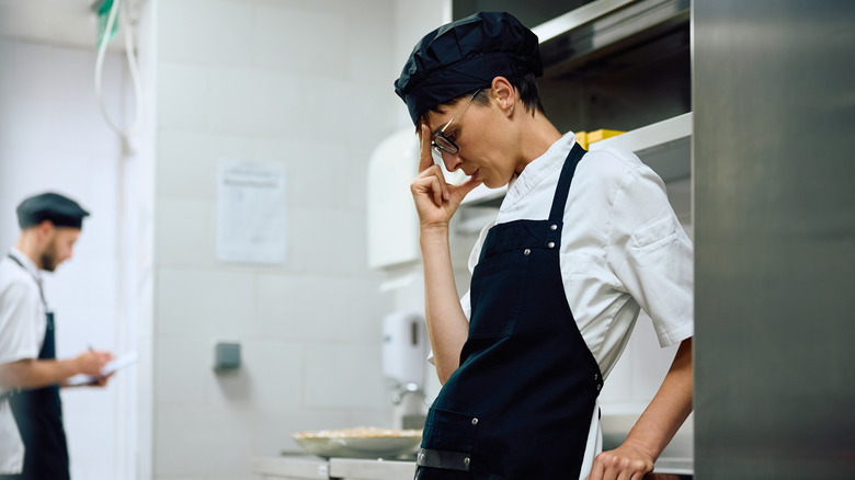A chef wearing an apron stresses in the kitchen