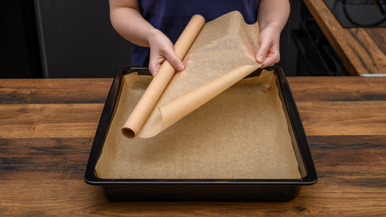 A person pulls a sheet of parchment paper to line a pan