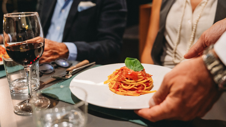 Waiter placing a plate of spaghetti in front of customer