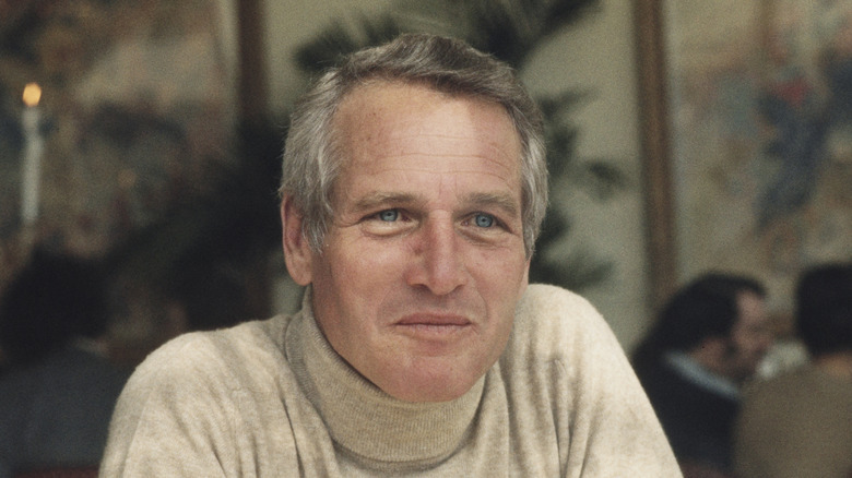Paul Newman in a beige turtleneck seated at a table in an upscale restaurant