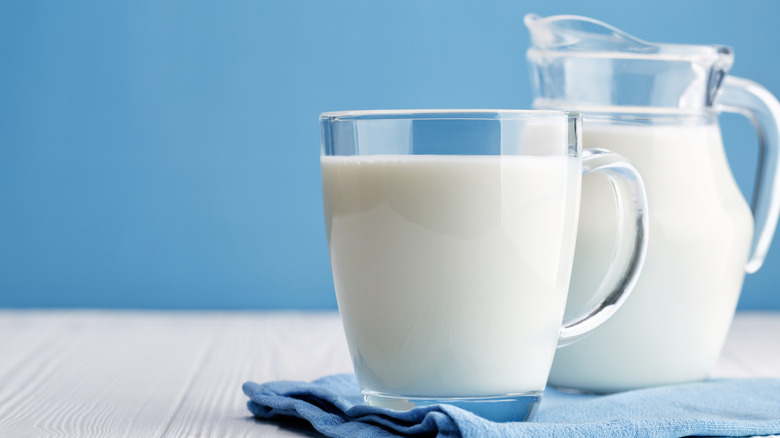 A glass jar and cup filled with milk, against a blue background
