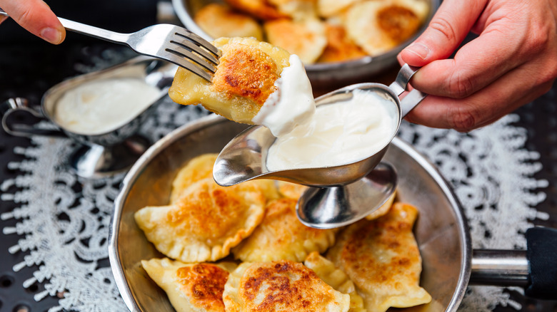 Person dipping pierogi into sour cream