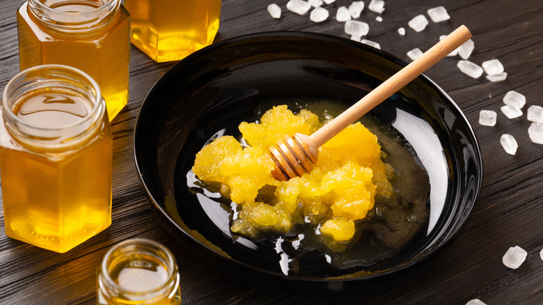 Jars of honey next to bowl of crystallized honey with dipper