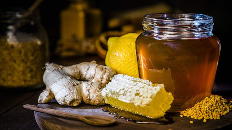 Jar of honey next to honeycomb, pollen, and ginger