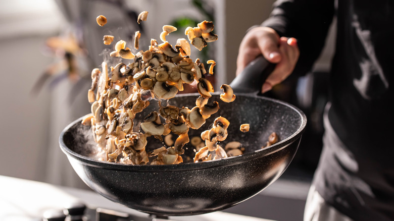 Chef flipping slicked mushrooms in black wok