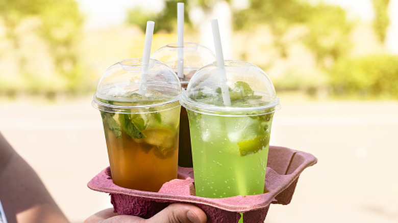 Hand holding tray of green cocktails in takeaway bubble-lid cups