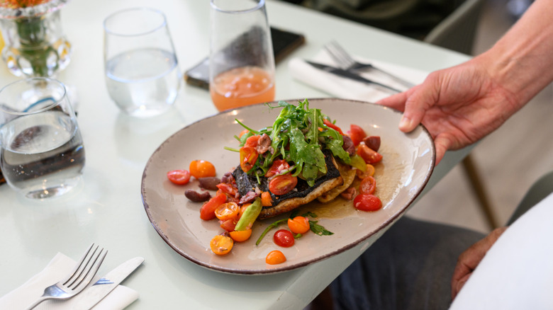 waiter serving plate of fish with cherry tomatoes