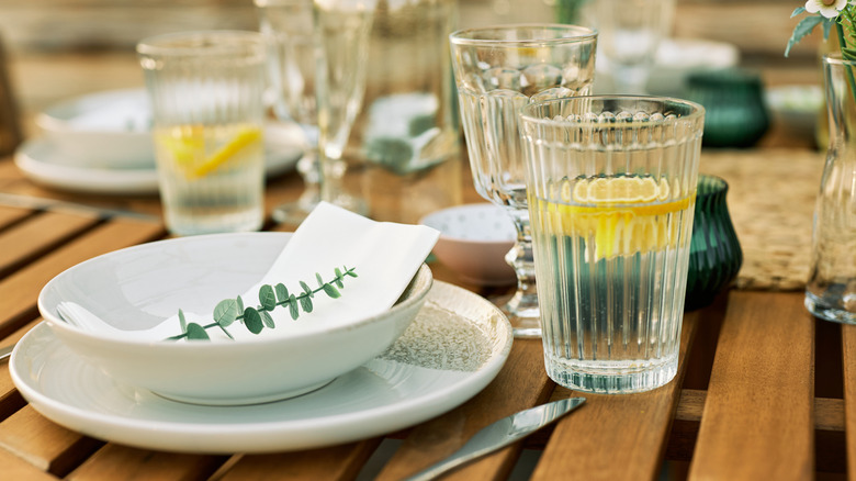 Outdoor table set with plates, bowls, cutlery, and glasses, including water with lemon