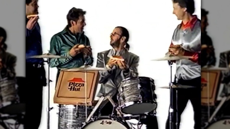 Ringo Starr sitting at a drum kit with a box of Pizza Hut pizza surrounded by the Monkees