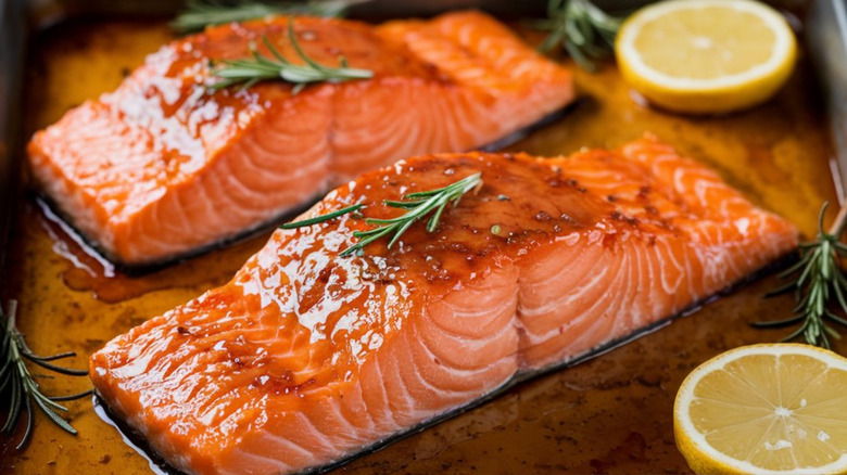 Two glistening salmon filets in a pan with rosemary and lemon slices