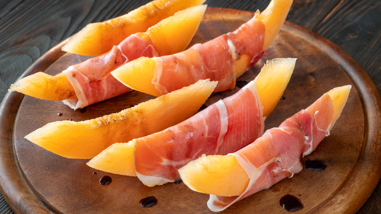 Melon wedges wrapped in prosciutto on a wooden platter
