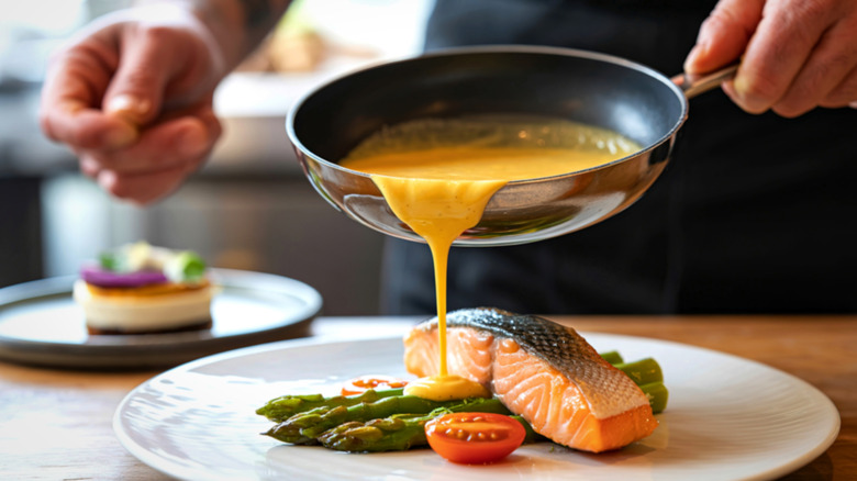 A person pouring sauce from a pan on a salmon plate