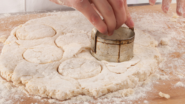 Person cutting out biscuit rounds dusted in flour on a cutting board