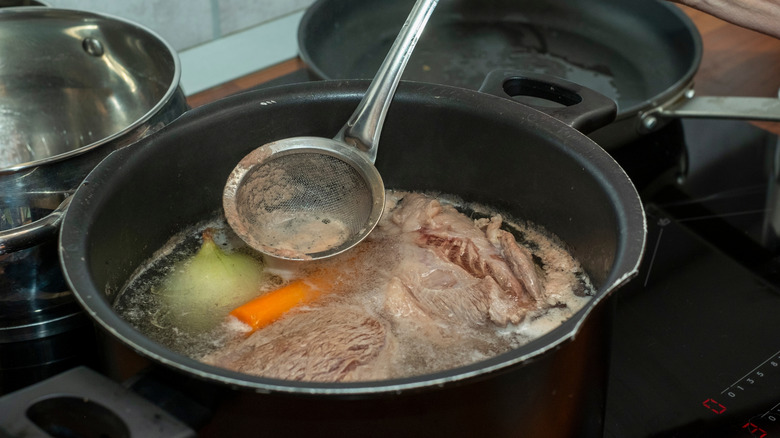 Skimming foam off pot of beef and vegetable stock