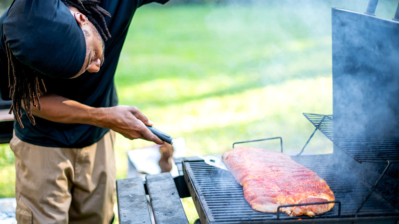 A pitmaster checking meat in a smoker
