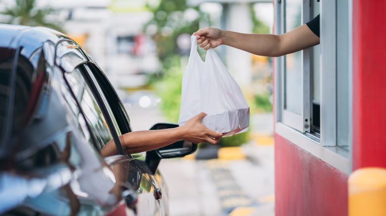 Customer receiving a fast food order in plastic bag from a drive-thru window
