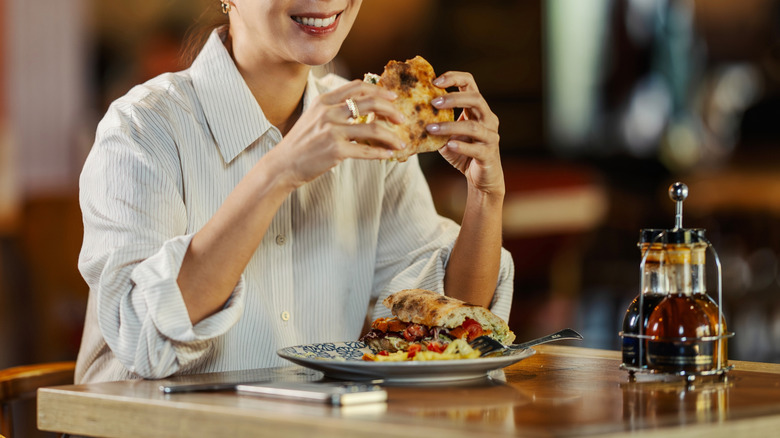 Smiling woman sitting alone at a restaurant, holding a burger
