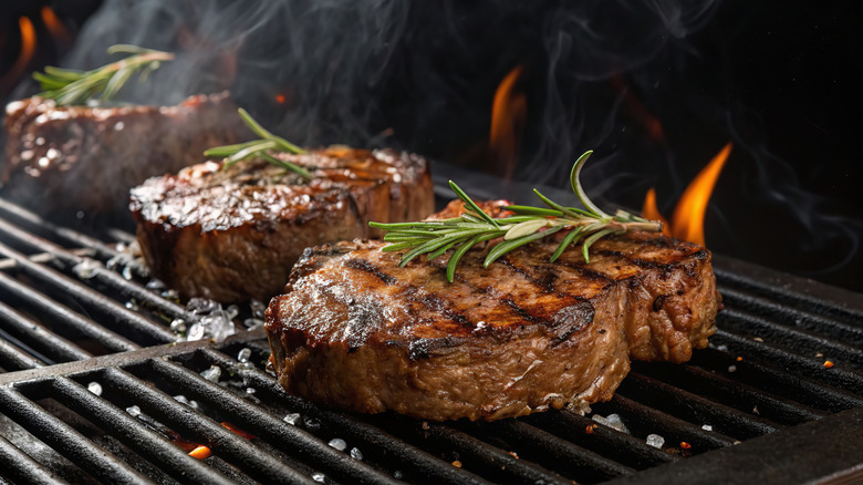 three steaks on a flaming grill with rosemary sprigs