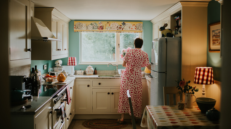 Woman in a dress standing at the sink of a small, vintage-styled kitchen