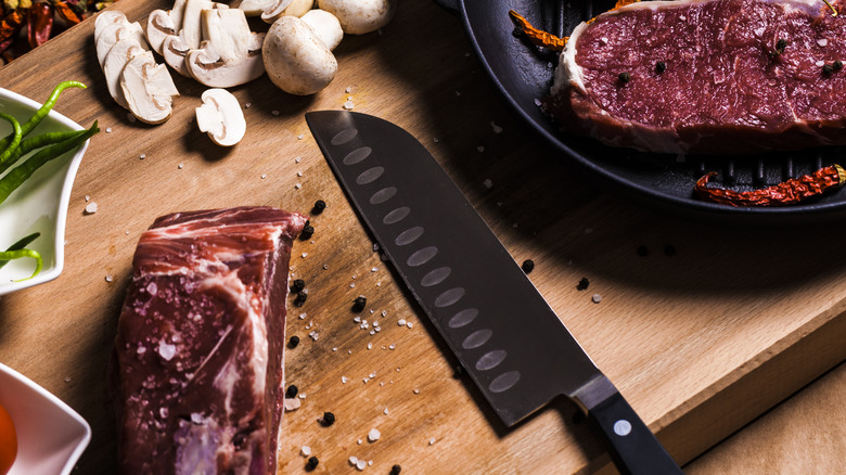 A Santoku knife beside pieces of meat and spices