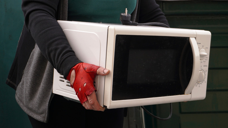 person with gloves on carrying microwave