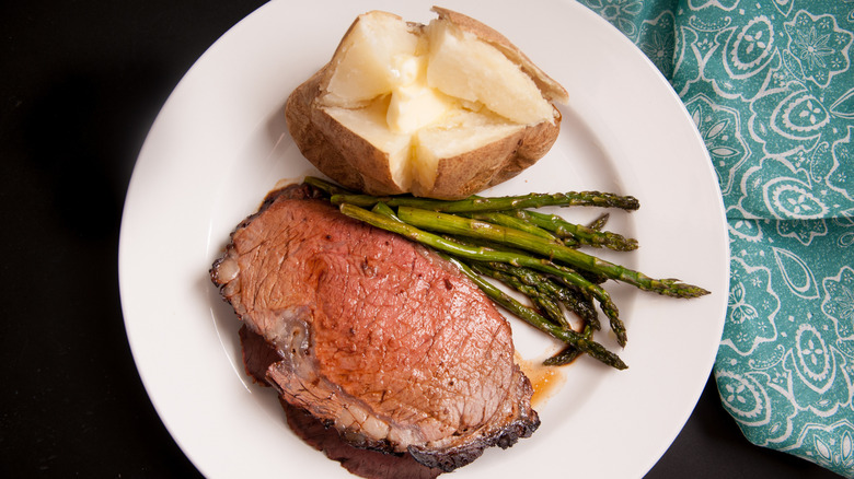 A plate featured prime rib, asparagus, and a baked potato