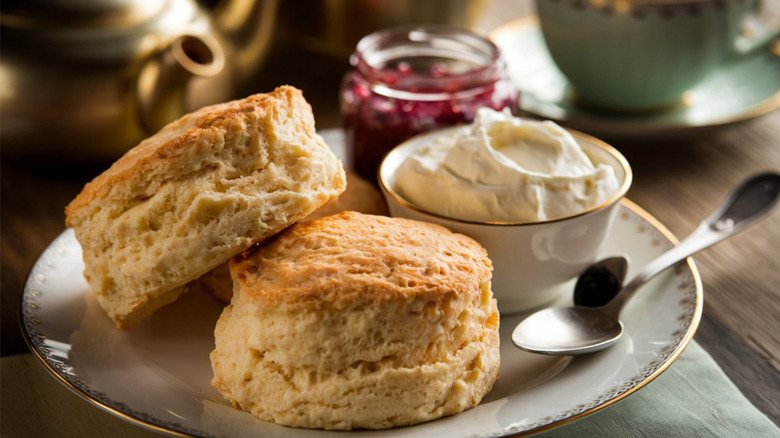 Scones, clotted cream, and jam on a white plate with a spoon.