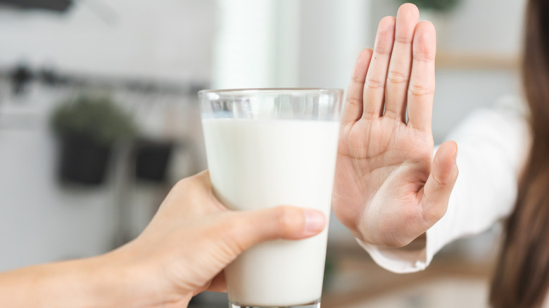 Someone holding their hand palm out to reject an offered glass of milk from another person
