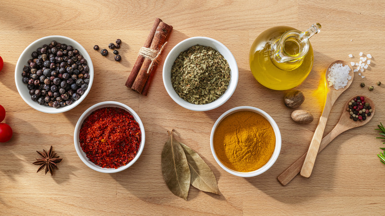 Various whole and ground spices in bowls and scattered on a wooden background