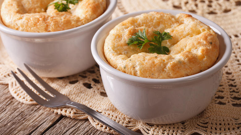 Two cheese soufflés baked in white ramekins and garnished with herbs