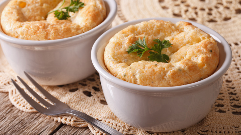 Two cheese soufflés baked in white ramekins and garnished with herbs